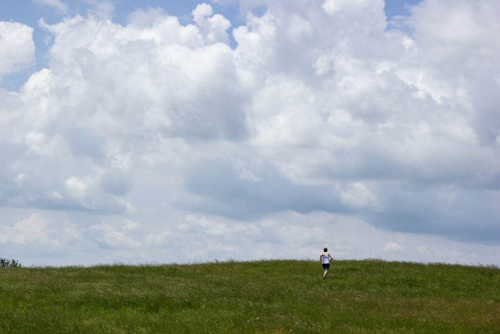 Ben running through a green grassy field under a sky full of cumulus clouds.