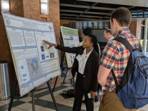 Jae gestures at her poster while presenting her research to a physicist at the SESAPS Conference