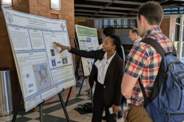 Jae gestures at her poster while presenting her research to a physicist at the SESAPS Conference